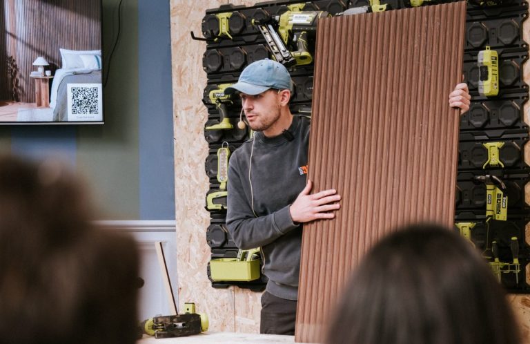 Presenter Laura Jane Clark giving a professional talk in front of a brand banner at an interior exhibition event.