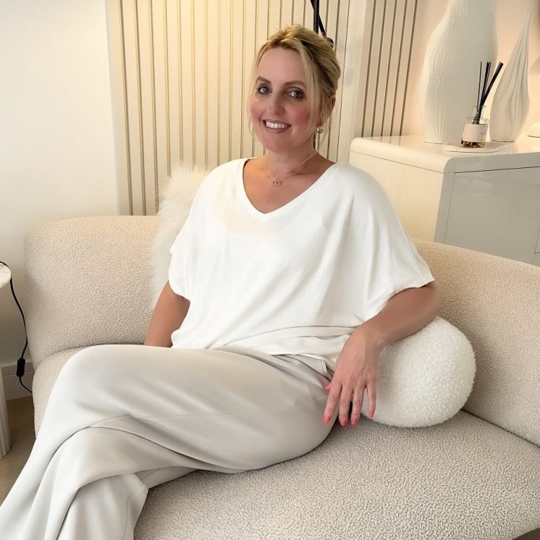 Portrait of Kate Sandhu smiling indoors in a white patterned t-shirt.